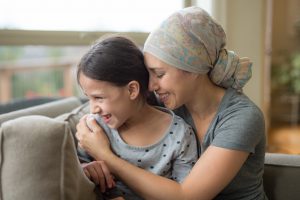 Ethnic young mom with cancer holding 8-year old daughter on couch